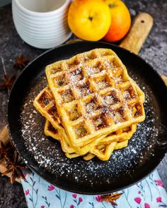 waffles on a plate with powdered sugar and oranges in the background