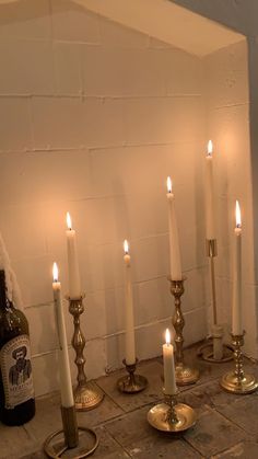 several candles are lit in front of a wine bottle on the floor next to a brick wall