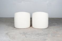 two white round stools sitting on top of a cement floor next to a wall