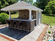 an outdoor bar with chairs around it in the middle of a yard and trees behind it