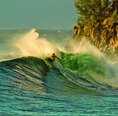 a man riding a wave on top of a surfboard in the ocean next to a cliff