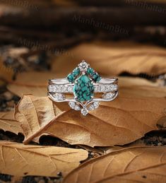 a turquoise and white stone ring sitting on top of a leaf covered ground with leaves around it