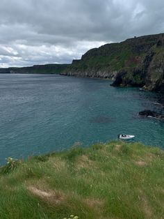 there is a small boat in the water at the edge of the cliff and grass on the shore