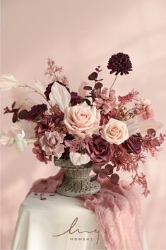 a vase filled with lots of flowers on top of a white cloth covered tablecloth