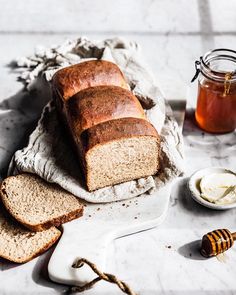 sliced loaf of bread sitting on top of a cutting board next to butter and honey