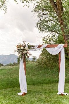 an outdoor wedding ceremony setup with white drapes and greenery on the grass, in front of a tree