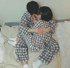 two people in pajamas are hugging on a bed