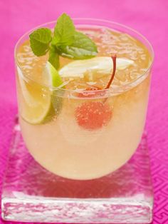 a close up of a drink in a glass on a pink table cloth with limes and strawberries