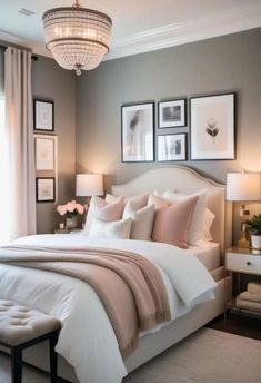 a white bed sitting under a chandelier next to two pictures on the wall