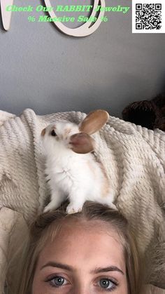 a woman laying on top of a bed next to a small white rabbit sitting on her head