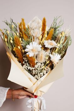 a woman holding a bouquet of flowers in her hand with white and gold accents on it