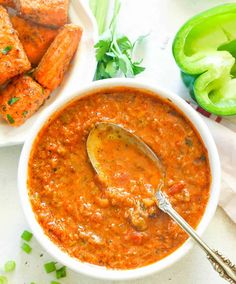 a white bowl filled with red chili sauce next to green onions and chicken wings on a plate