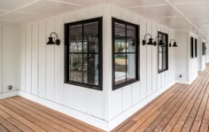 the front porch of a house with white walls and wood flooring is lined with black windows