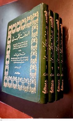 four green books with arabic writing on them sitting on a shelf next to a wall