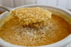 a spoon with some food in it on top of a white bowl filled with soup