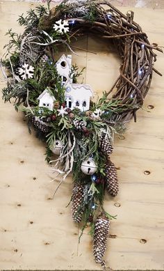 a christmas wreath with pine cones and white houses on it, sitting on a wooden table