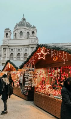 people are walking around an outdoor market with christmas decorations on display in front of a large building