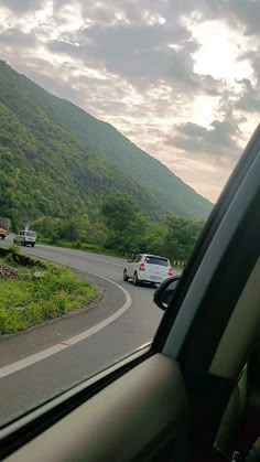 two cars driving down the road in front of a mountain