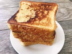 a grilled cheese sandwich on a white plate with wood table in the back ground