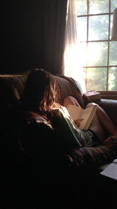 a person sitting on a couch with a book in their lap and sunlight coming through the window