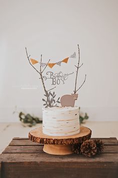 a white cake with an animal topper sitting on a wooden table next to pine cones