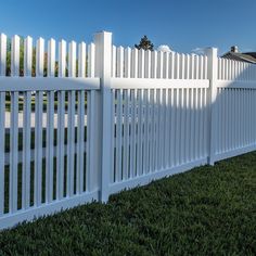 a white picket fence with grass in the foreground and blue sky in the background