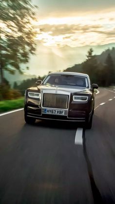 a rolls royce driving down the road at sunset