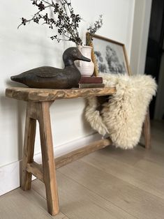 a duck statue sitting on top of a wooden bench next to a vase with flowers