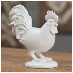 a white rooster figurine sitting on top of a wooden table