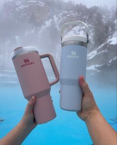 two people holding up their mugs in front of a blue pool with snow on the ground