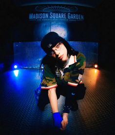 a young man sitting on the ground in front of a blue and black background with lights