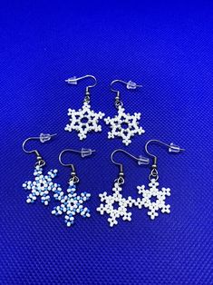 six snowflake earrings are shown on a blue background, one is white and the other is silver