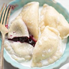 two dumplings with blueberry sauce and a fork in a bowl on a table