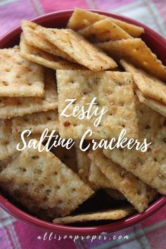 a red bowl filled with crackers on top of a checkered table cloth and the words zesty saltine crackers above it