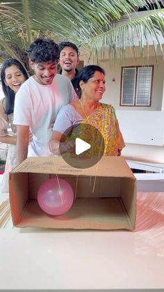 a group of people standing around a box with a pink ball in it and an object inside