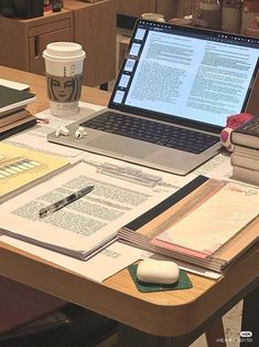 an open laptop computer sitting on top of a wooden desk next to a cup of coffee