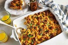 a casserole dish with meat and cheese in it on a table next to two glasses of orange juice