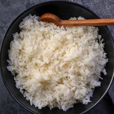 rice in a black bowl with a wooden spoon on the side and a gray cloth