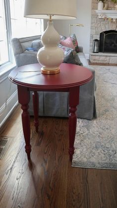 a red table with a white lamp on it in front of a couch and fireplace