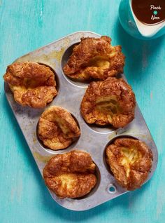 several pastries in a muffin tin next to a cup of coffee on a blue table