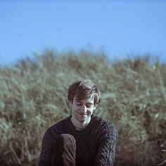 a man sitting on the ground in front of tall grass