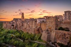 the sun is setting over an old city in italy, with trees and buildings on either side