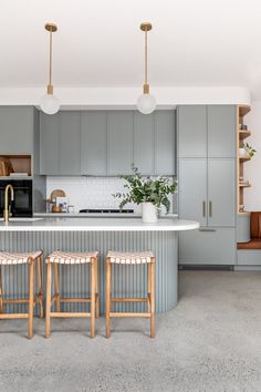 two stools sit in front of an island with marble countertops and gray cabinets