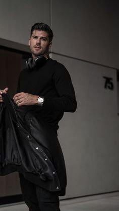 a man in black is holding a leather bag and looking at the camera while wearing headphones