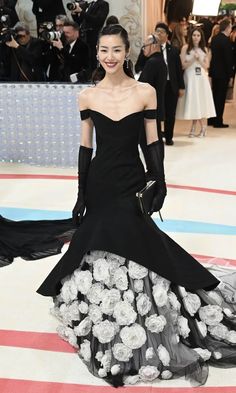 a woman in a black dress and gloves standing on a red, white, and blue carpet