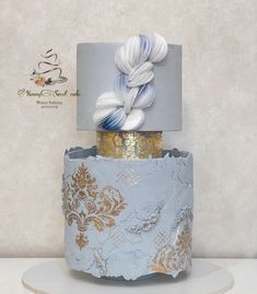 a three tiered blue and gold wedding cake with white flowers on the top layer