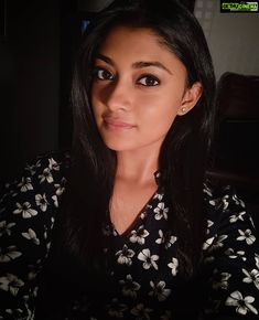 a woman with long black hair is looking at the camera while wearing a floral shirt