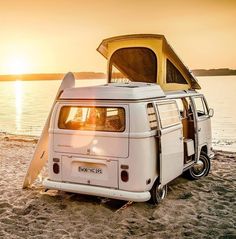 an old camper van is parked on the beach with its surfboard propped up against it