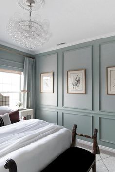 a bed sitting in a bedroom next to two pictures on the wall and a chandelier above it