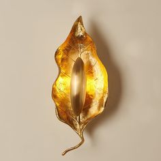 a golden leaf shaped object is hanging on the wall with a light bulb in it's center